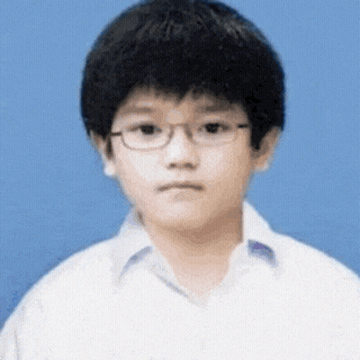 A Young Boy Wearing Glasses And A White Shirt Looks At The Camera . GIF