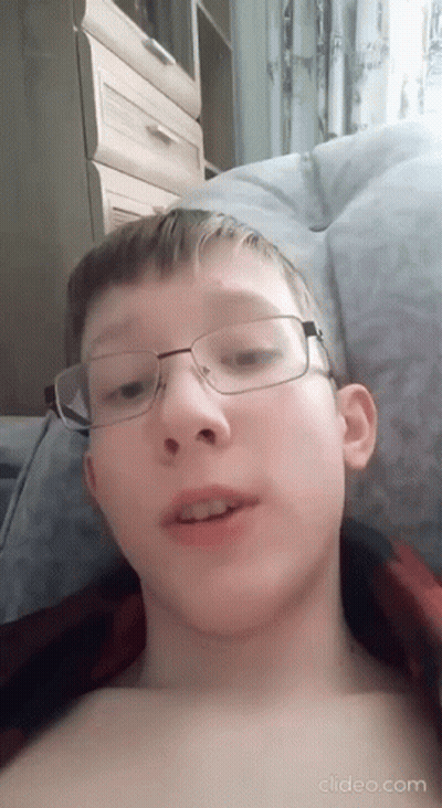 A Young Boy Wearing Glasses Is Laying On A Bed Without A Shirt . GIF