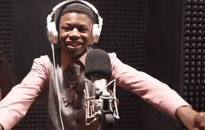 A Young Boy Wearing Headphones And A Pink Shirt Is Standing In Front Of A Microphone GIF