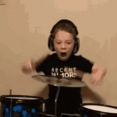 A Young Boy Wearing Headphones Is Playing Drums And Making A Funny Face . GIF