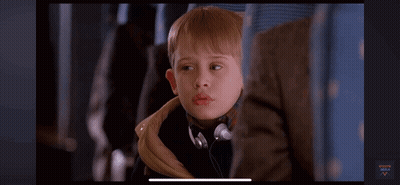 A Young Boy Wearing Headphones Is Sitting On A Plane And Looking At The Camera . GIF