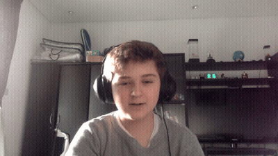 A Young Boy Wearing Headphones Looks At The Camera In Front Of A Digital Clock That Reads 9:06 GIF