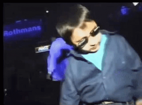 Boy In Blue Shirt Dancing In Front Of Rothmans Sign GIF