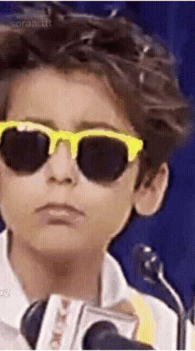 A Young Boy Wearing Sunglasses And A Microphone . GIF
