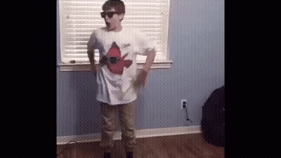 A Young Boy Wearing Sunglasses And A White Shirt Is Standing In Front Of A Window In A Room . GIF