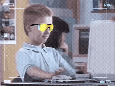 A Young Boy Wearing Sunglasses Is Sitting In Front Of A Computer Monitor GIF