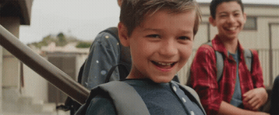 A Young Boy With A Backpack Is Smiling For The Camera While Sitting On The Stairs . GIF