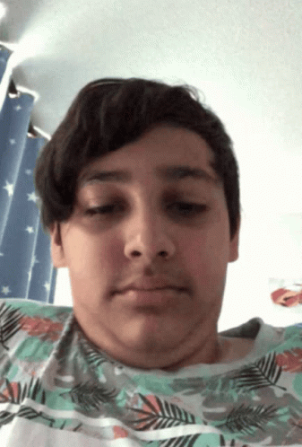 A Young Boy With A Floral Shirt On Looks At The Camera With His Eyes Closed GIF