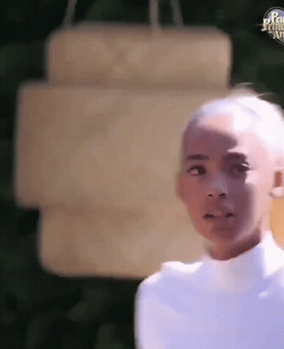A Young Boy With A Shaved Head Is Standing In Front Of A Sign . GIF