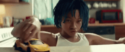 A Young Boy With Blue Hair Is Playing With A Toy Car On A Kitchen Counter . GIF