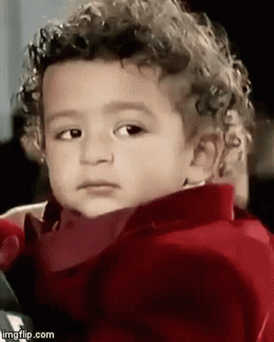 A Young Boy With Curly Hair Is Wearing A Red Jacket And Making A Funny Face . GIF