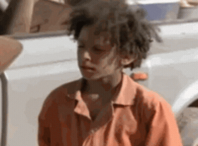 A Young Boy With Dreadlocks Is Standing Next To A White Truck . GIF
