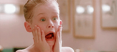A Young Boy With His Mouth Open And His Hands On His Face Looks Surprised GIF