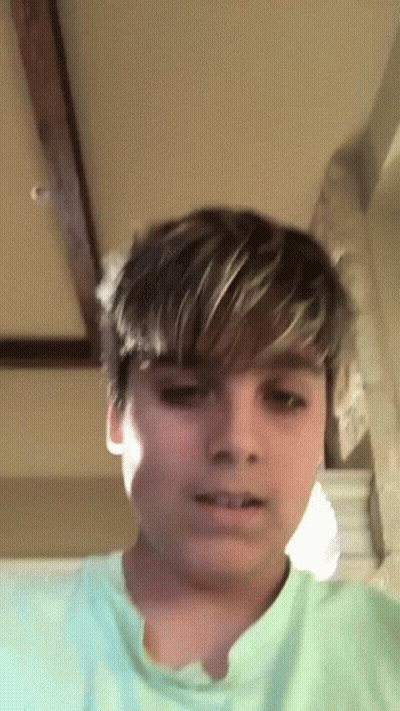 A Young Boy With Short Hair Is Wearing A Green Shirt . GIF