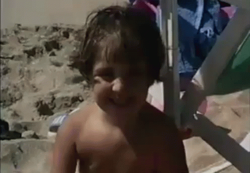 A Young Boy Without A Shirt Is Standing On The Beach GIF