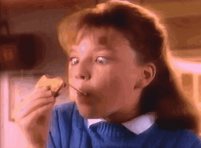A Young Girl In A Blue Sweater Is Eating A Piece Of Food GIF