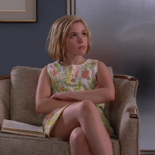 A Young Girl In A Floral Dress Sits In A Chair With Her Eyes Closed GIF
