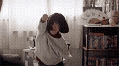 A Young Girl Is Dancing In A Room With A Fan . GIF