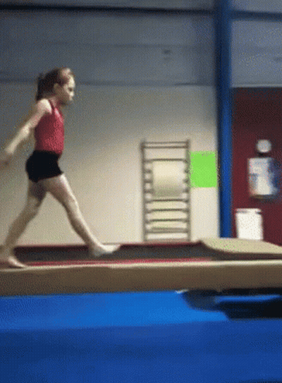 A Young Girl Is Doing A Trick On A Balance Beam In A Gym GIF