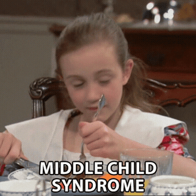 A Young Girl Is Sitting At A Table With A Fork In Her Mouth And The Words Middle Child Syndrome Written Above Her GIF