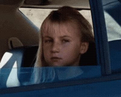 A Young Girl Is Sitting In A Blue Car Looking Out The Window . GIF