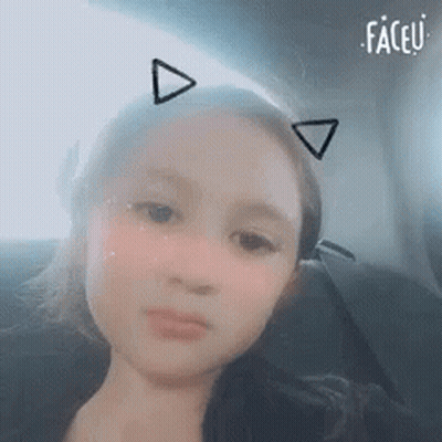 A Young Girl Is Sitting In A Car Wearing Cat Ears . GIF