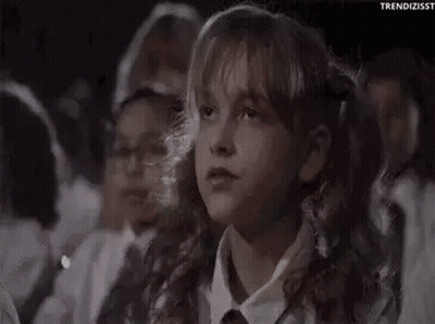 A Young Girl Is Sitting In A Crowd Of People Watching A Movie And Covering Her Mouth With Her Hand . GIF