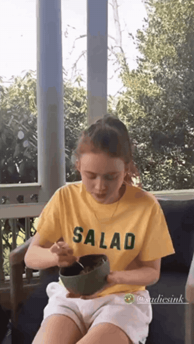A Young Girl Is Sitting On A Porch Eating A Salad From A Bowl . GIF
