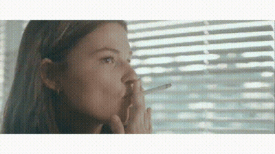A Young Girl Is Smoking A Cigarette In Front Of A Window . GIF
