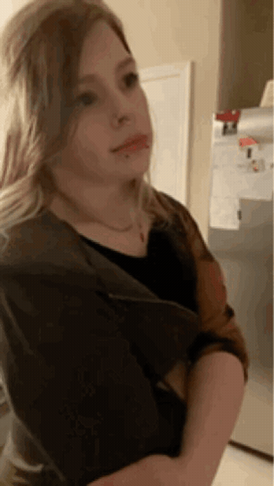 A Young Girl Is Standing In Front Of A Refrigerator And Looking At The Camera . GIF