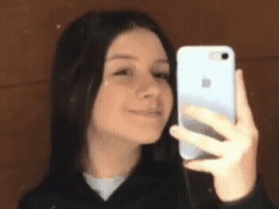 A Young Girl Is Taking A Selfie With Her Phone In Front Of A Mirror . GIF