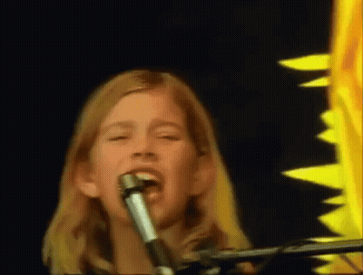 A Young Girl Singing Into A Microphone In Front Of A Sunflower GIF