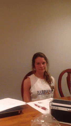A Young Girl Wearing A Barbado Shirt Sits At A Table GIF