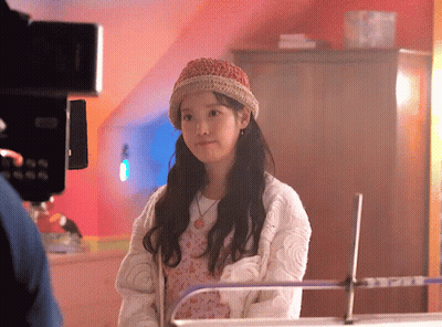 A Young Girl Wearing A Knitted Hat And A White Sweater Is Standing In Front Of A Camera . GIF