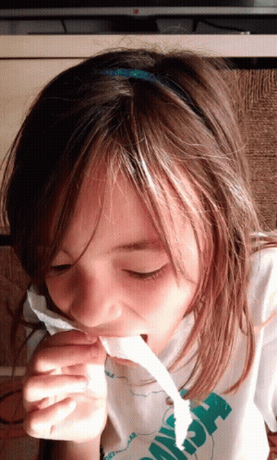 A Young Girl Wearing A Shirt That Says ' Hawaii ' On It Is Chewing On A Piece Of Paper GIF