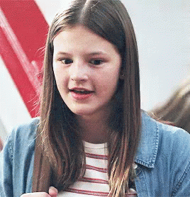 A Young Girl Wearing A Striped Shirt And A Denim Jacket Is Looking At The Camera . GIF