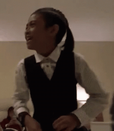 A Young Girl Wearing A Vest And A Bow Tie Is Dancing In A Room . GIF