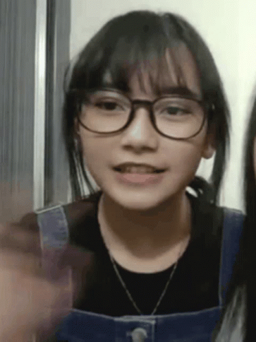 A Young Girl Wearing Glasses And Overalls Is Talking To Another Girl . GIF
