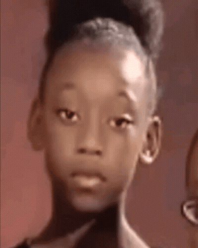 A Young Girl With A Bun On Her Head Is Looking At The Camera With A Sad Look On Her Face . GIF
