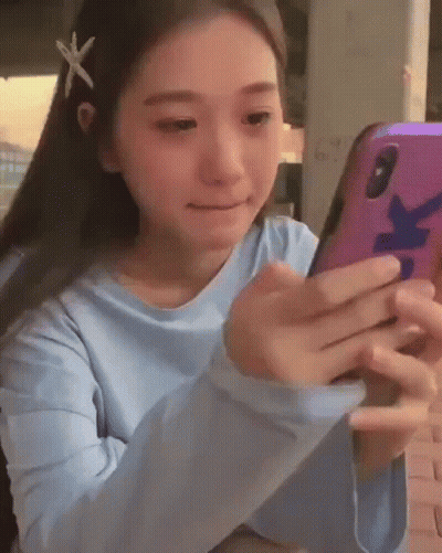 A Young Girl With A Starfish In Her Hair Is Looking At Her Cell Phone . GIF