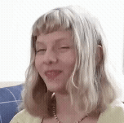 A Young Girl With Blonde Hair And A Necklace Is Smiling . GIF