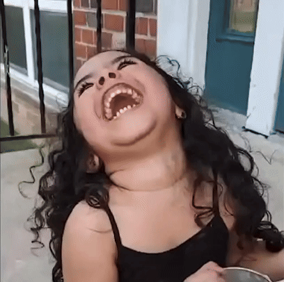 A Young Girl With Curly Hair Is Laughing With Her Mouth Wide Open GIF