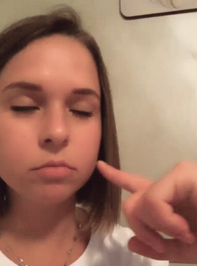 A Young Girl With Her Eyes Closed Is Pointing At Her Face GIF