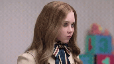 A Young Girl With Long Hair And A Bow Tie Is Standing In Front Of A Row Of Toys . GIF