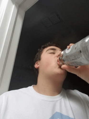 A Young Man Drinking From A Bottle With A Label That Says Vodka GIF