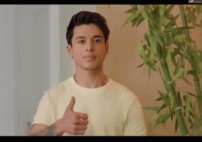 A Young Man Giving A Thumbs Up In Front Of A Bamboo Plant GIF