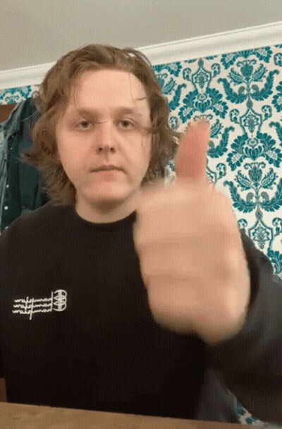 A Young Man Giving A Thumbs Up In Front Of A Wallpaper GIF