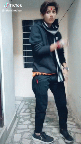 A Young Man In A Black Hoodie And Black Pants Is Standing In A Hallway With A Tik Tok Watermark On The Bottom Right GIF