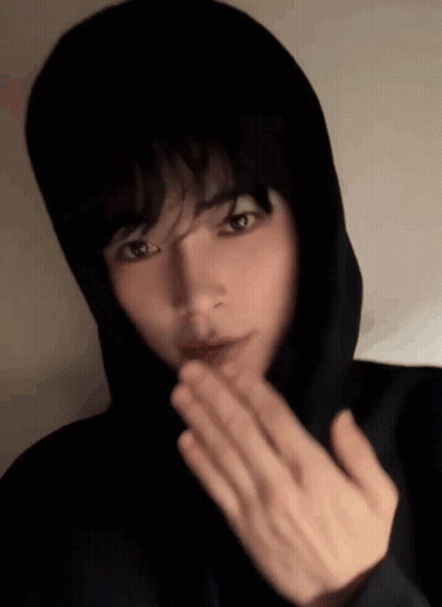 A Young Man In A Black Hoodie Is Blowing A Kiss GIF