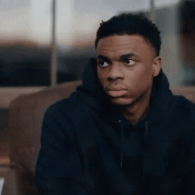 A Young Man In A Black Hoodie Is Sitting On A Couch Looking At Something . GIF